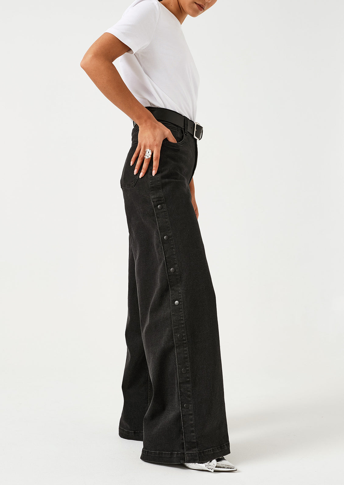A woman wearing a pair of black wide leg jeans with windbreaker-style snap detail along outer leg.