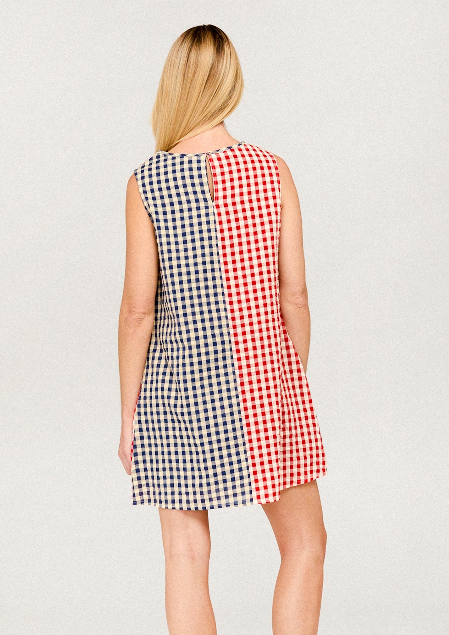 Woman wearing a sleeveless dress with a red, white, and blue checkered pattern on a plain background