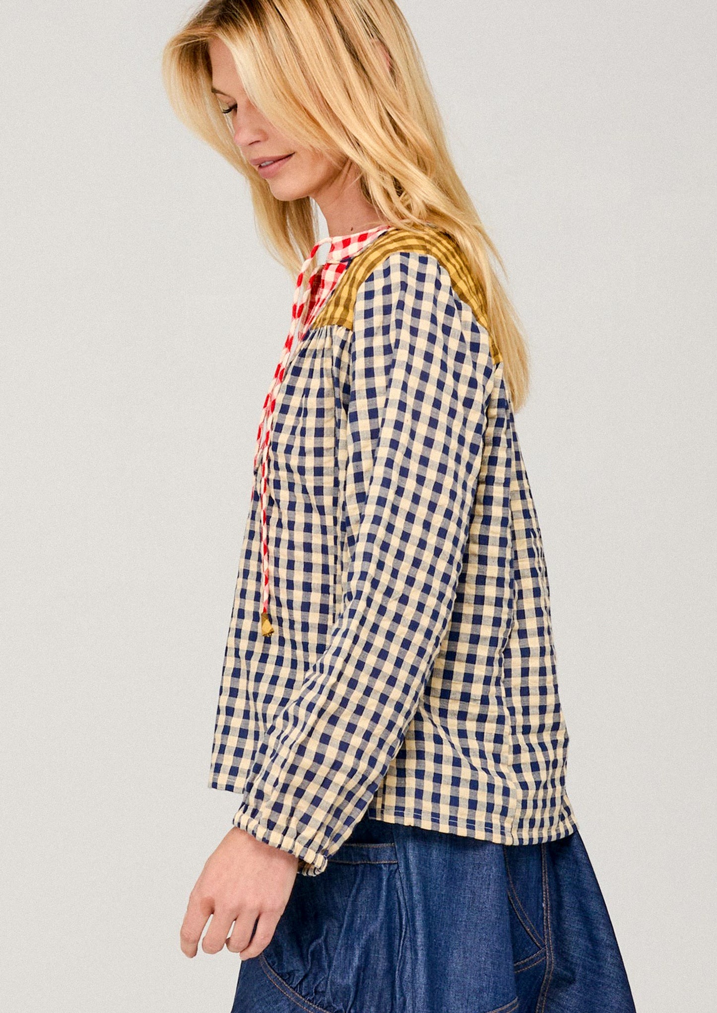 Woman wearing a blue and white checkered shirt with a red plaid scarf on a light gray background