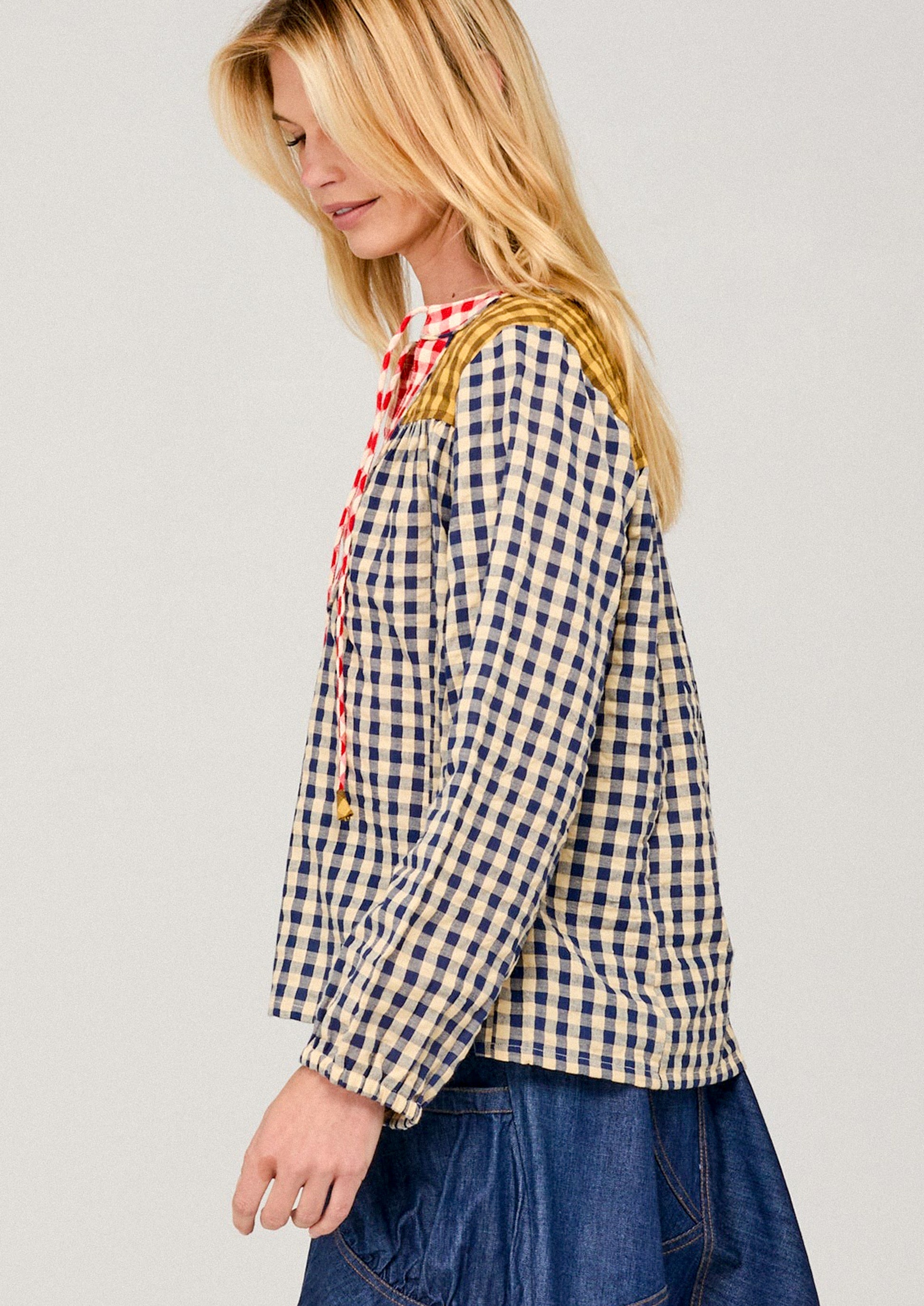 Woman wearing a blue and white checkered shirt with a red plaid scarf on a light gray background