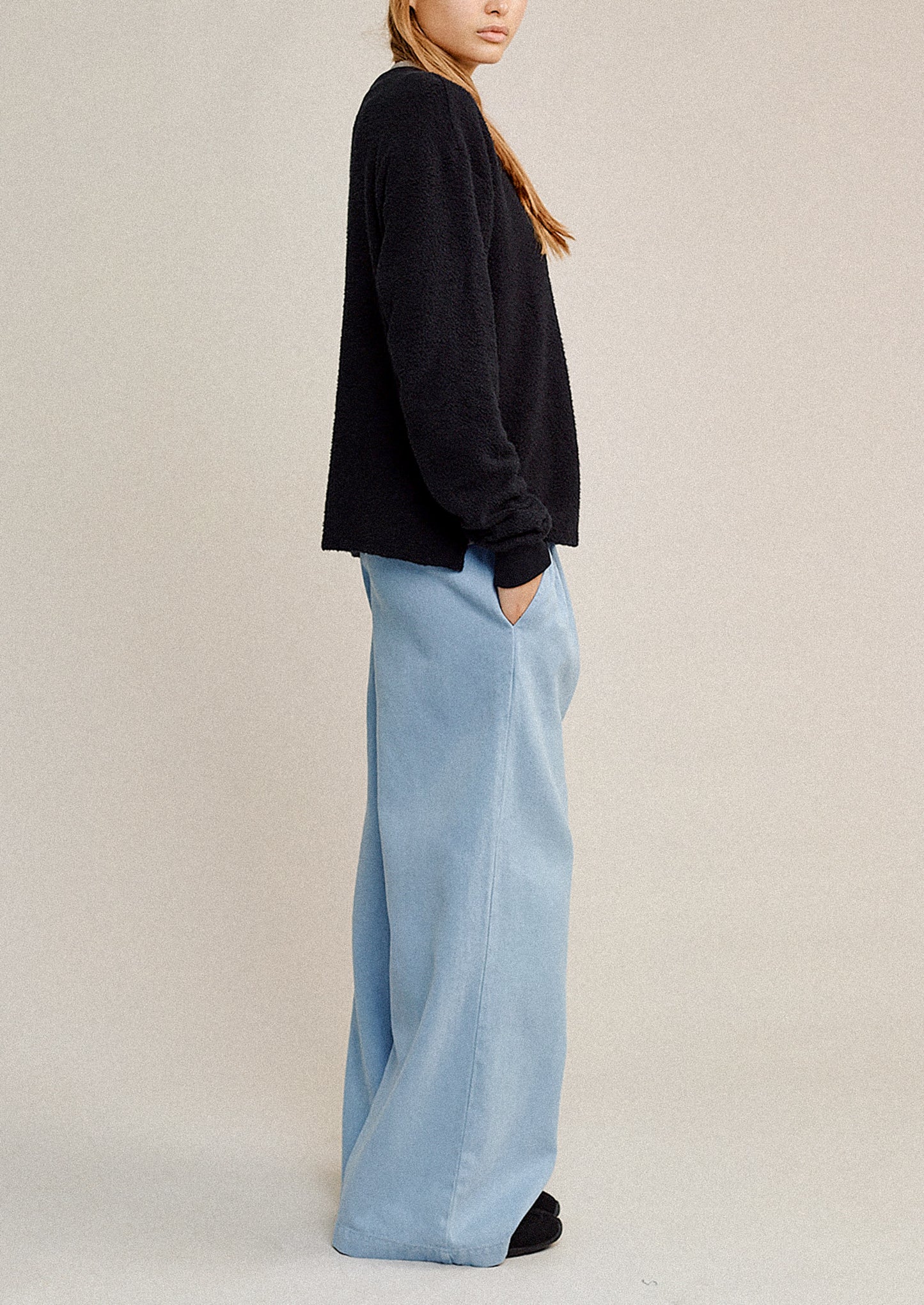 Person wearing a black sweater and light blue pants on a beige background