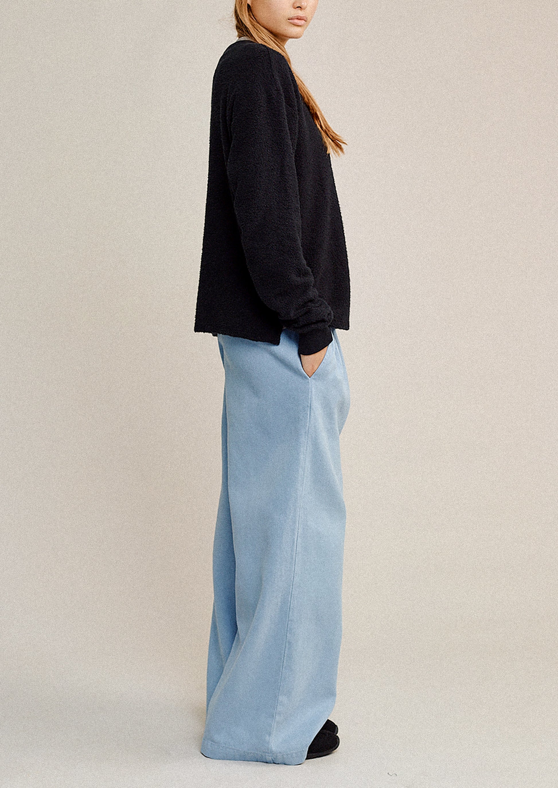 Person wearing a black sweater and light blue pants on a beige background