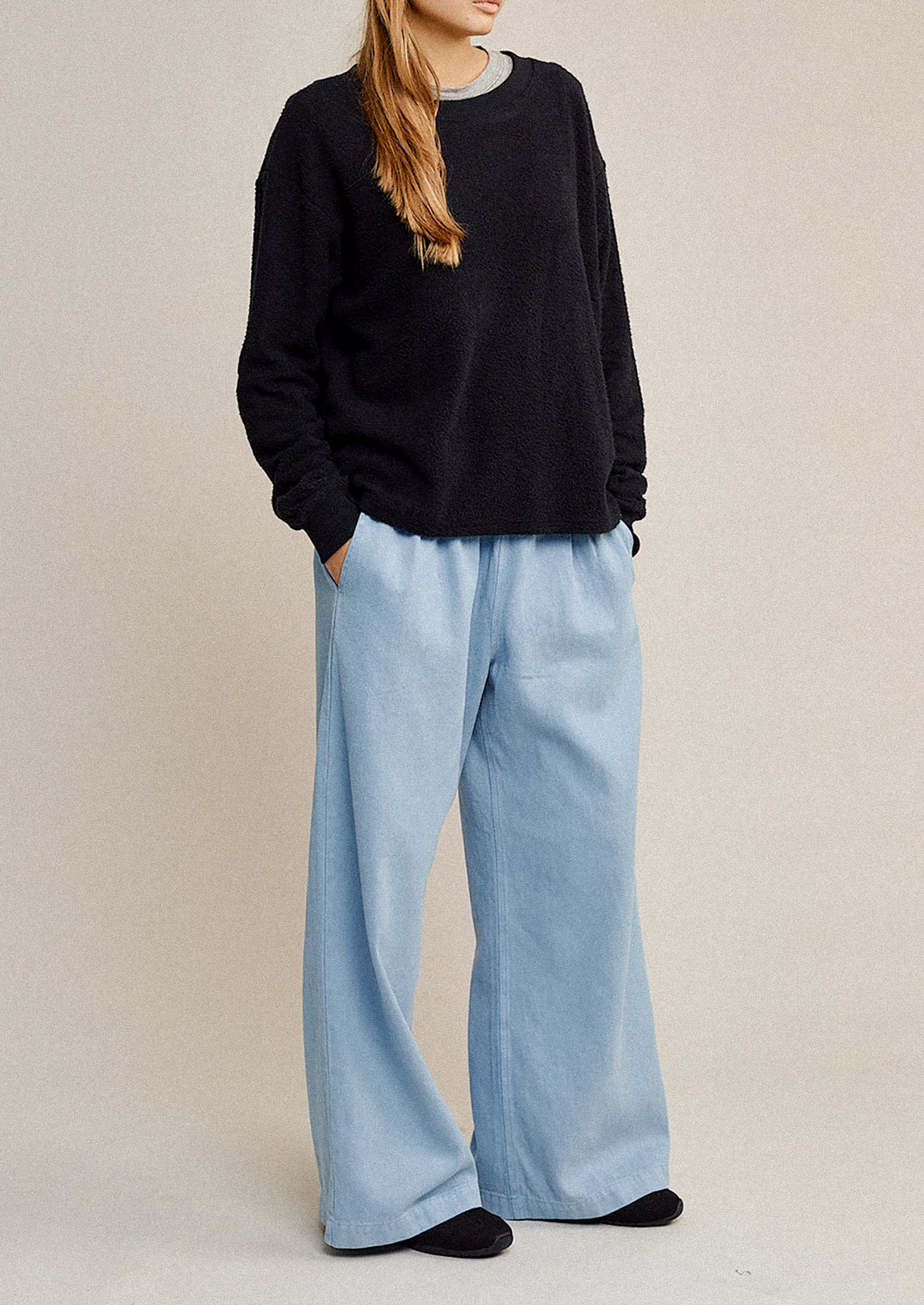 Person wearing a black sweater and light blue pants on a beige background