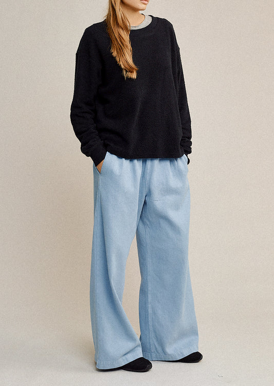 Person wearing a black sweater and light blue pants on a beige background