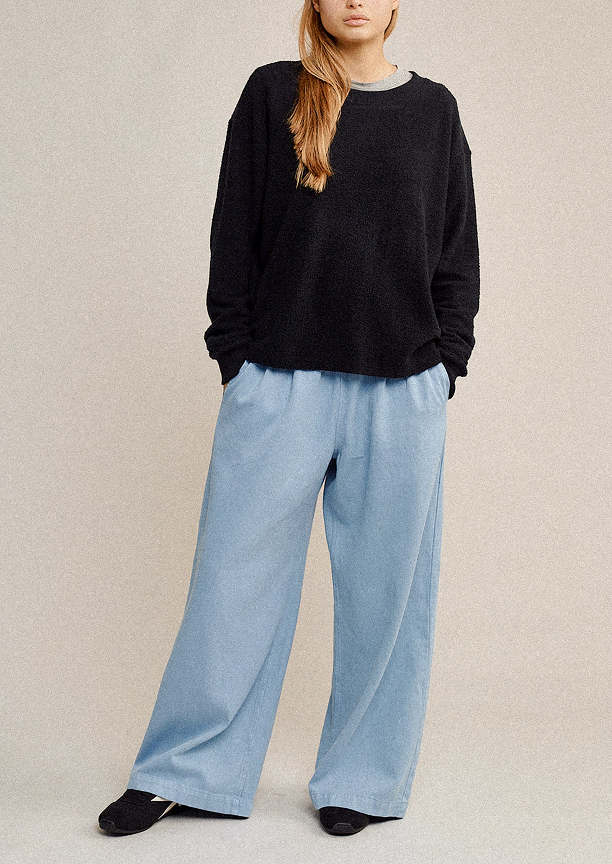 Person wearing a black sweater and light blue pants on a beige background