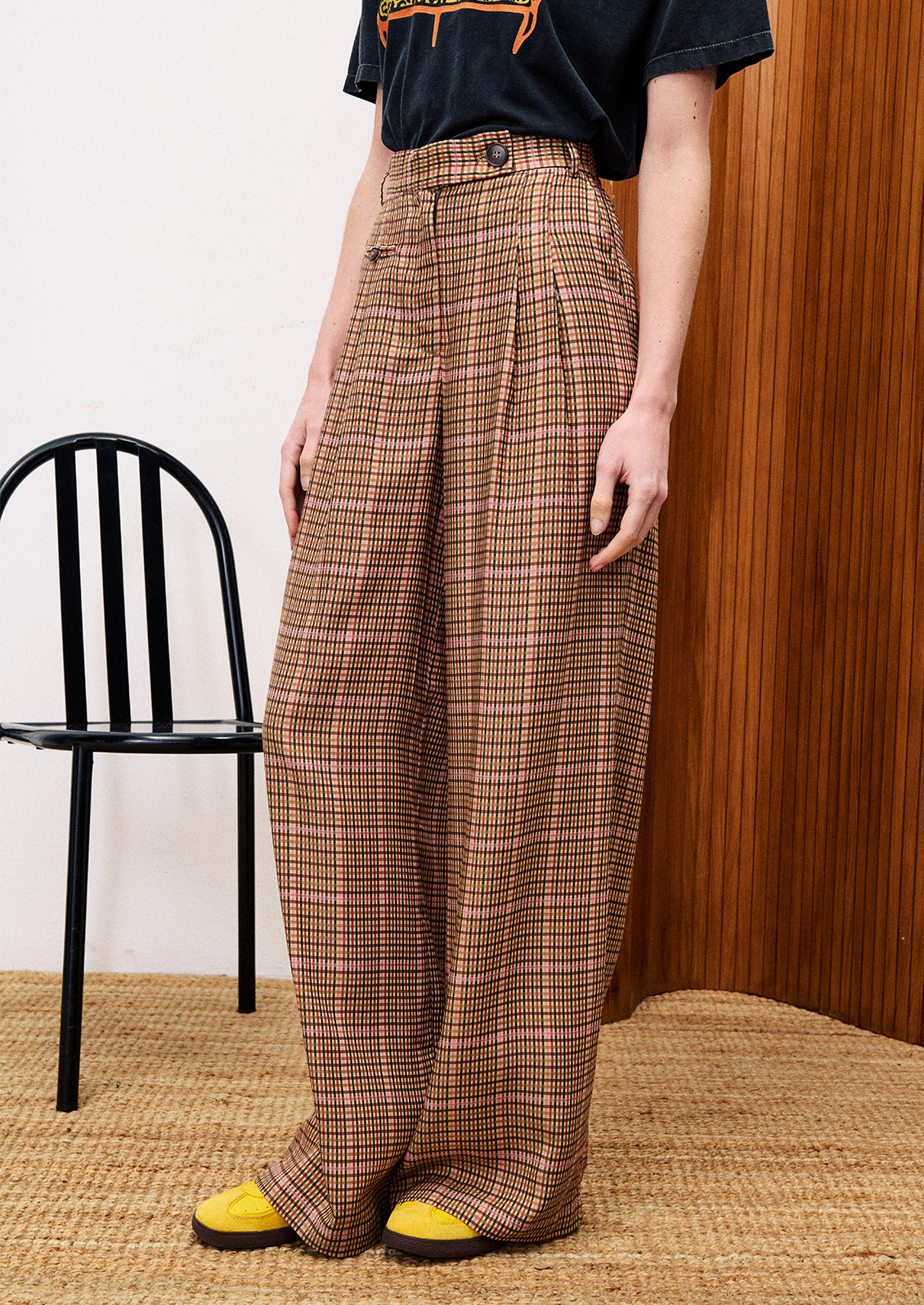 Person wearing plaid pants with a black chair and wooden wall in the background