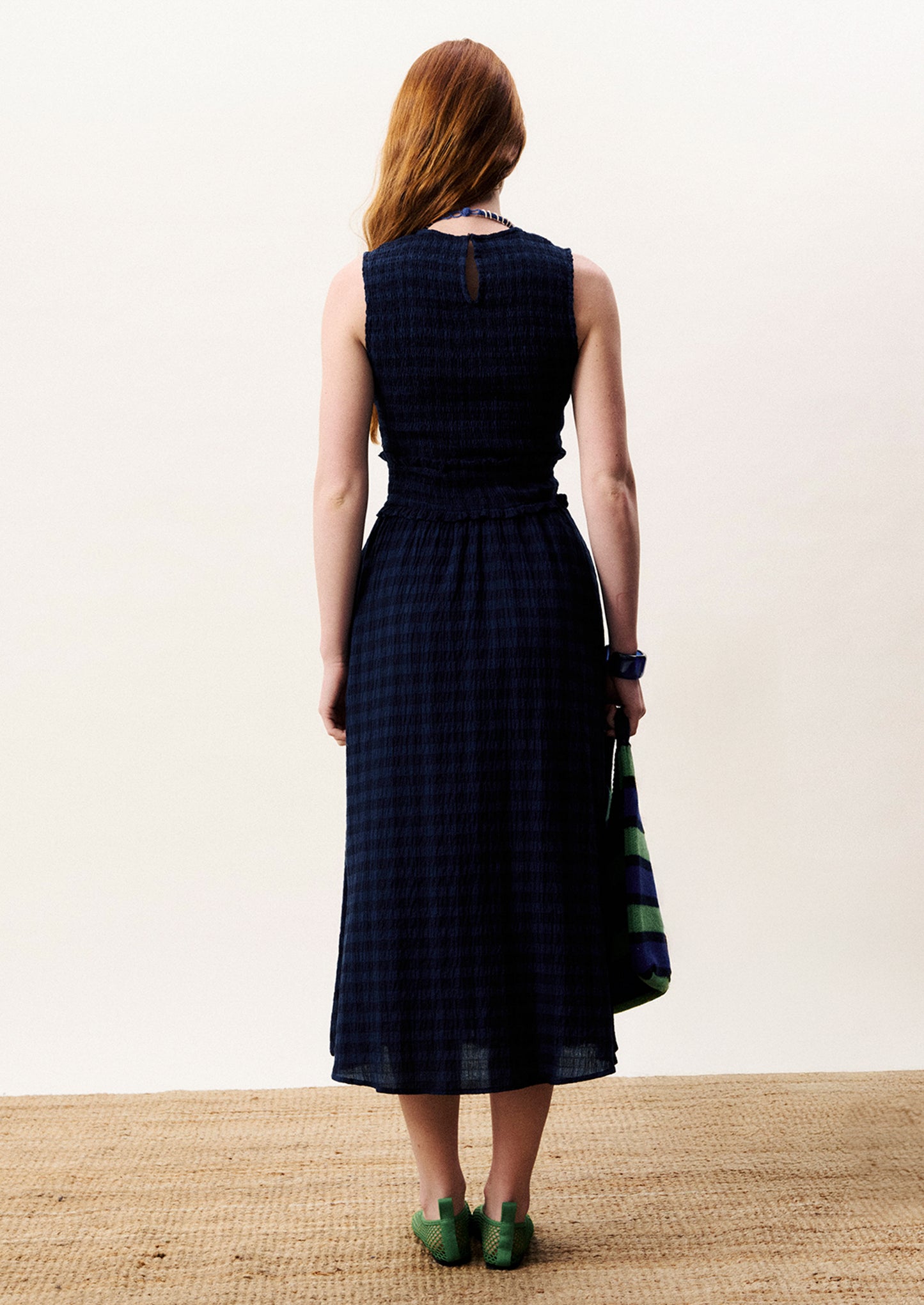 Woman wearing a dark blue checkered dress standing on a textured surface with a white background