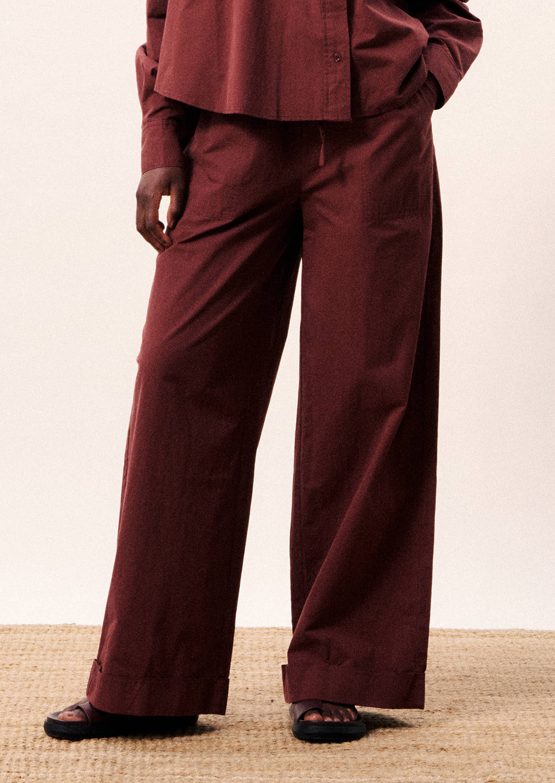 A person wearing a pair of wide leg cotton pants in wine color.