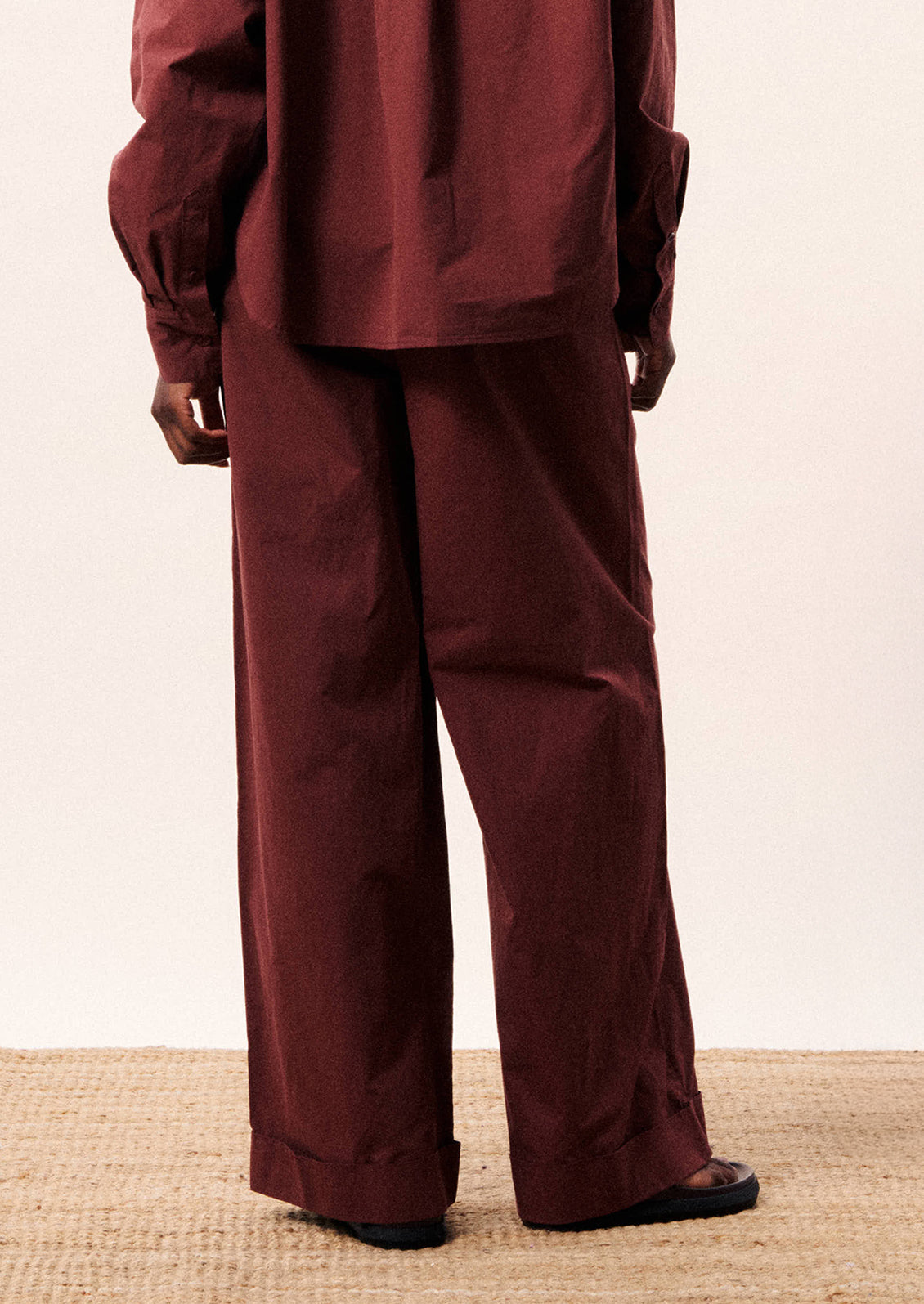 A person wearing a pair of wide leg cotton pants in wine color.