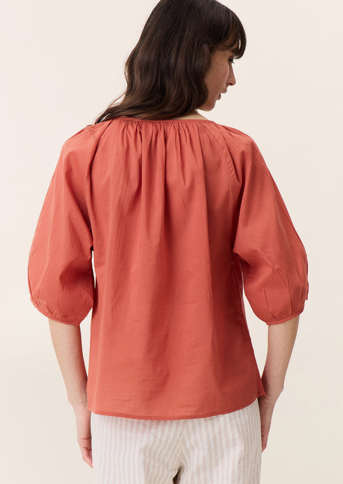 A woman wearing a short sleeve blouse in coral red color with shirring at neckline.
