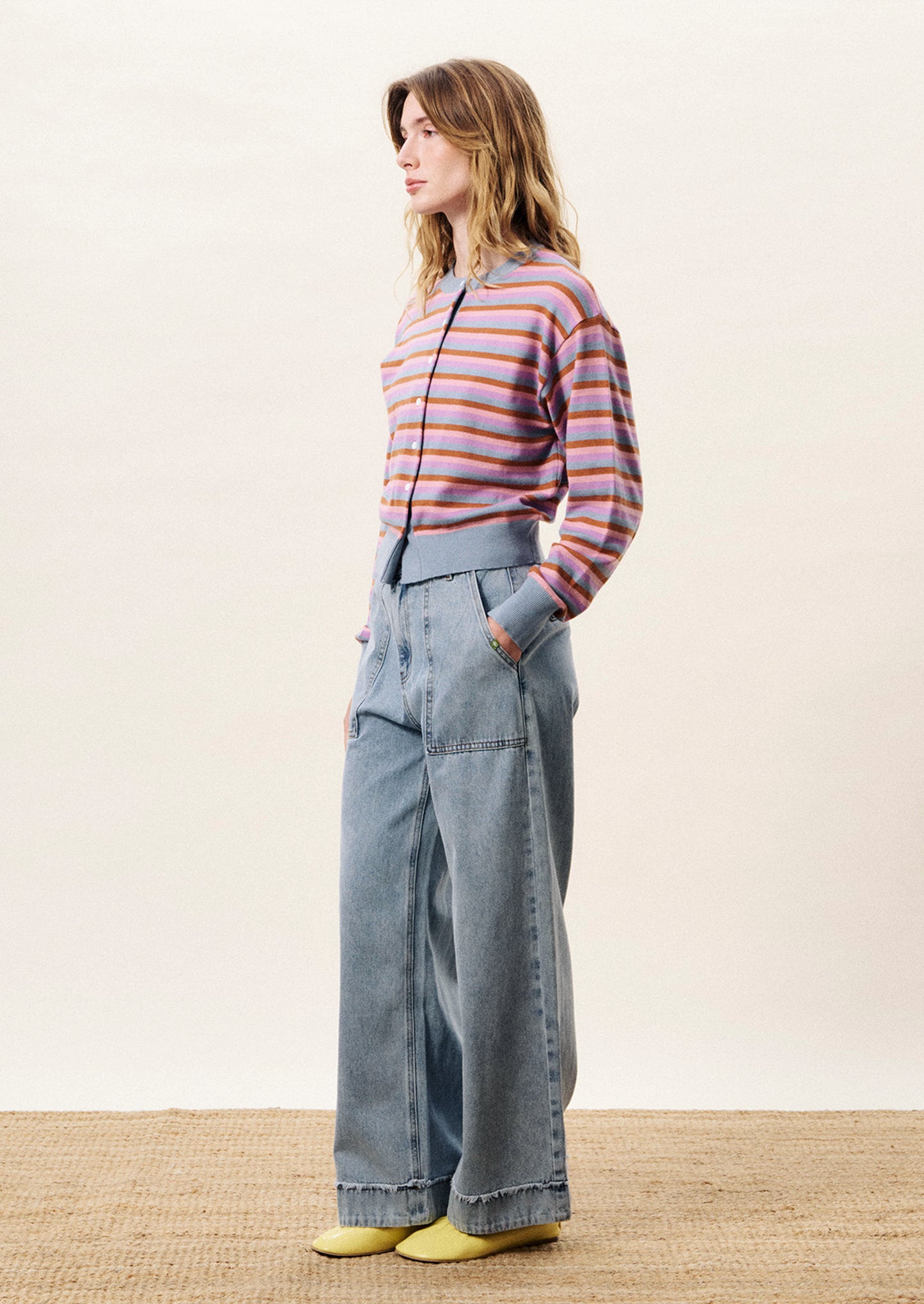 Woman wearing a striped sweater and wide-leg jeans against a plain background