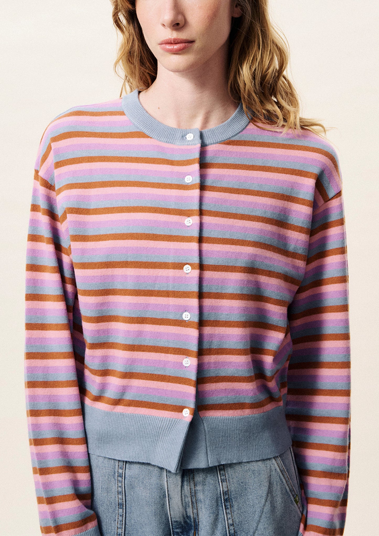 Person wearing a striped sweater with pastel and brown colors on a plain background