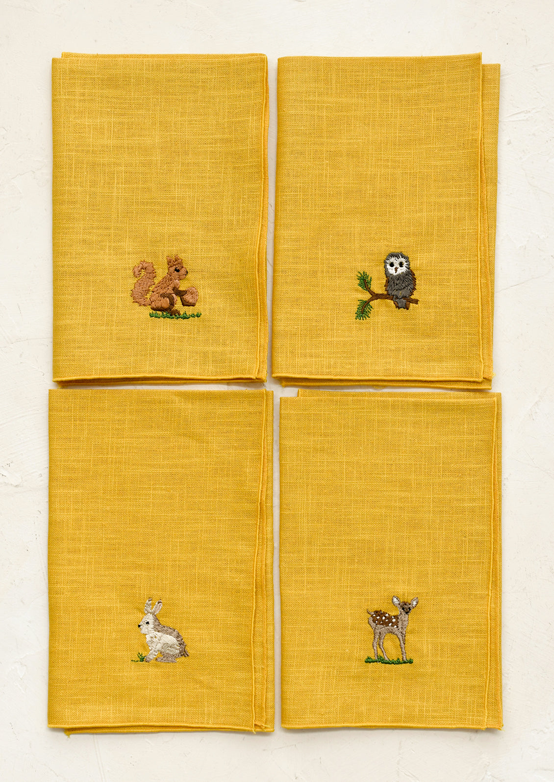 Four yellow napkins with embroidered animal designs on a white background
