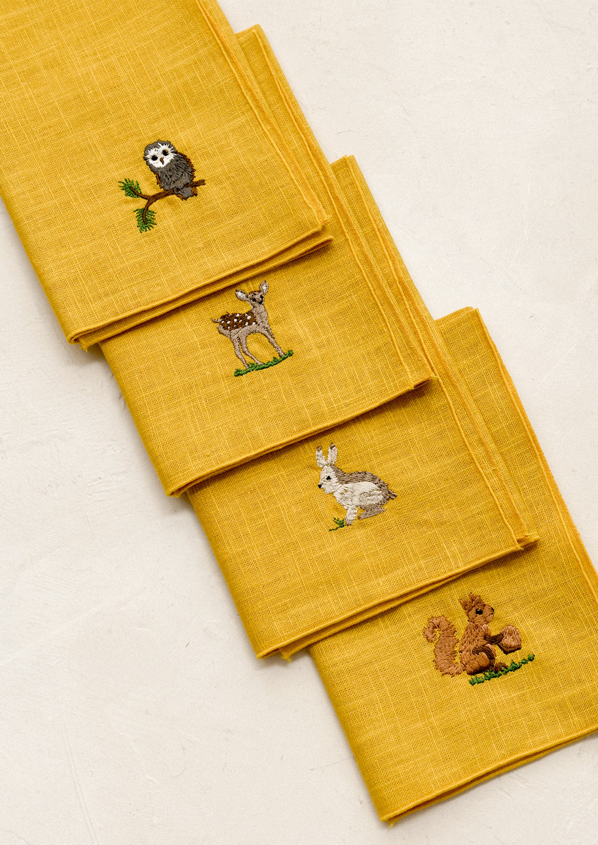 Set of yellow napkins with embroidered animal designs on a light beige background