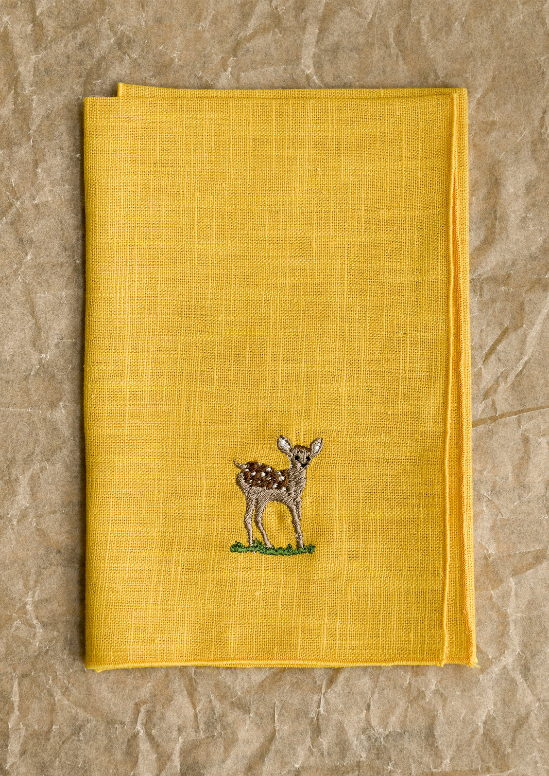 Yellow fabric napkin with an embroidered deer design.