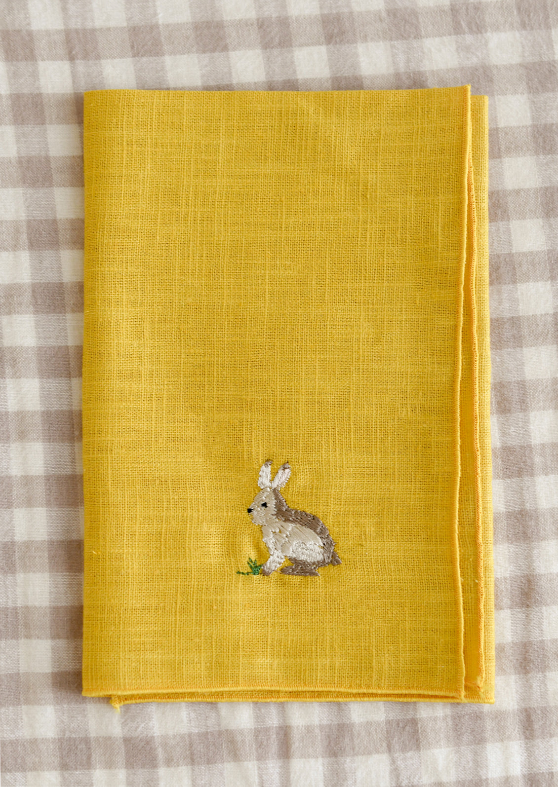 Yellow napkin with embroidered rabbit design on a checkered tablecloth