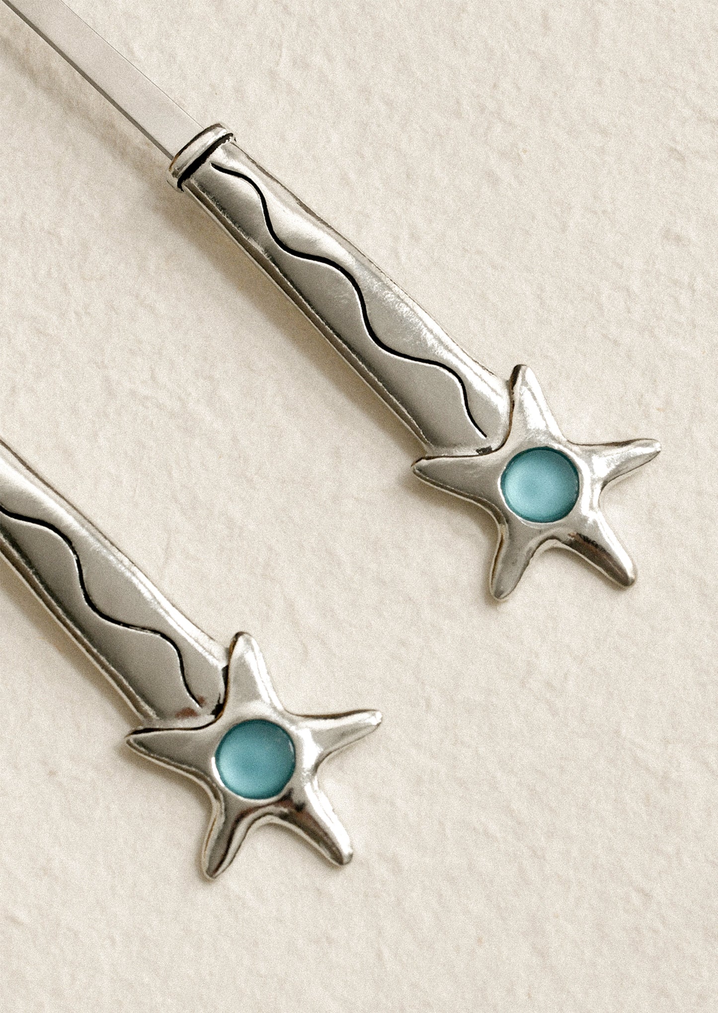 Silver star-shaped earrings with turquoise centers on a beige background