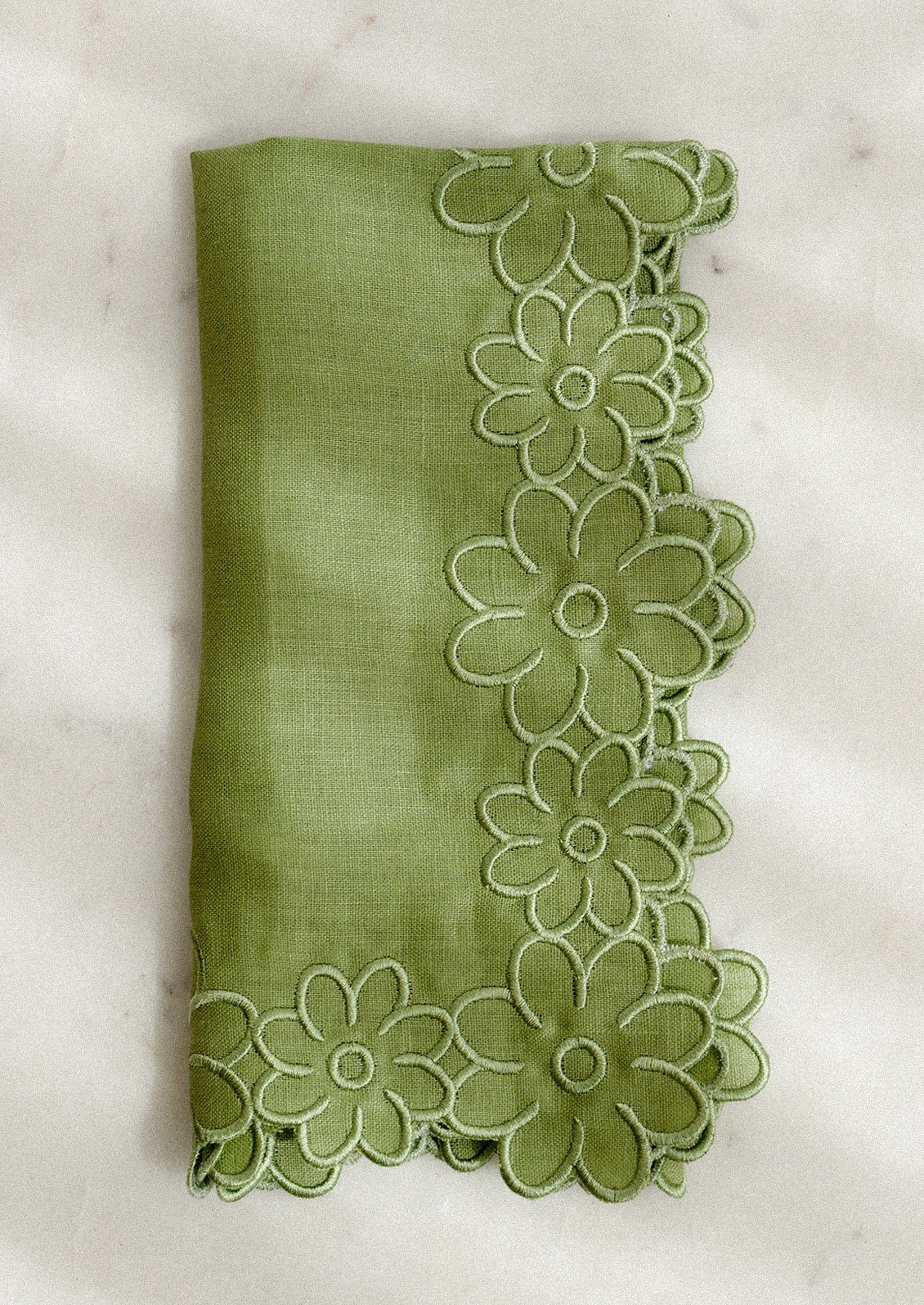 Green fabric napkin with floral trim on a white background