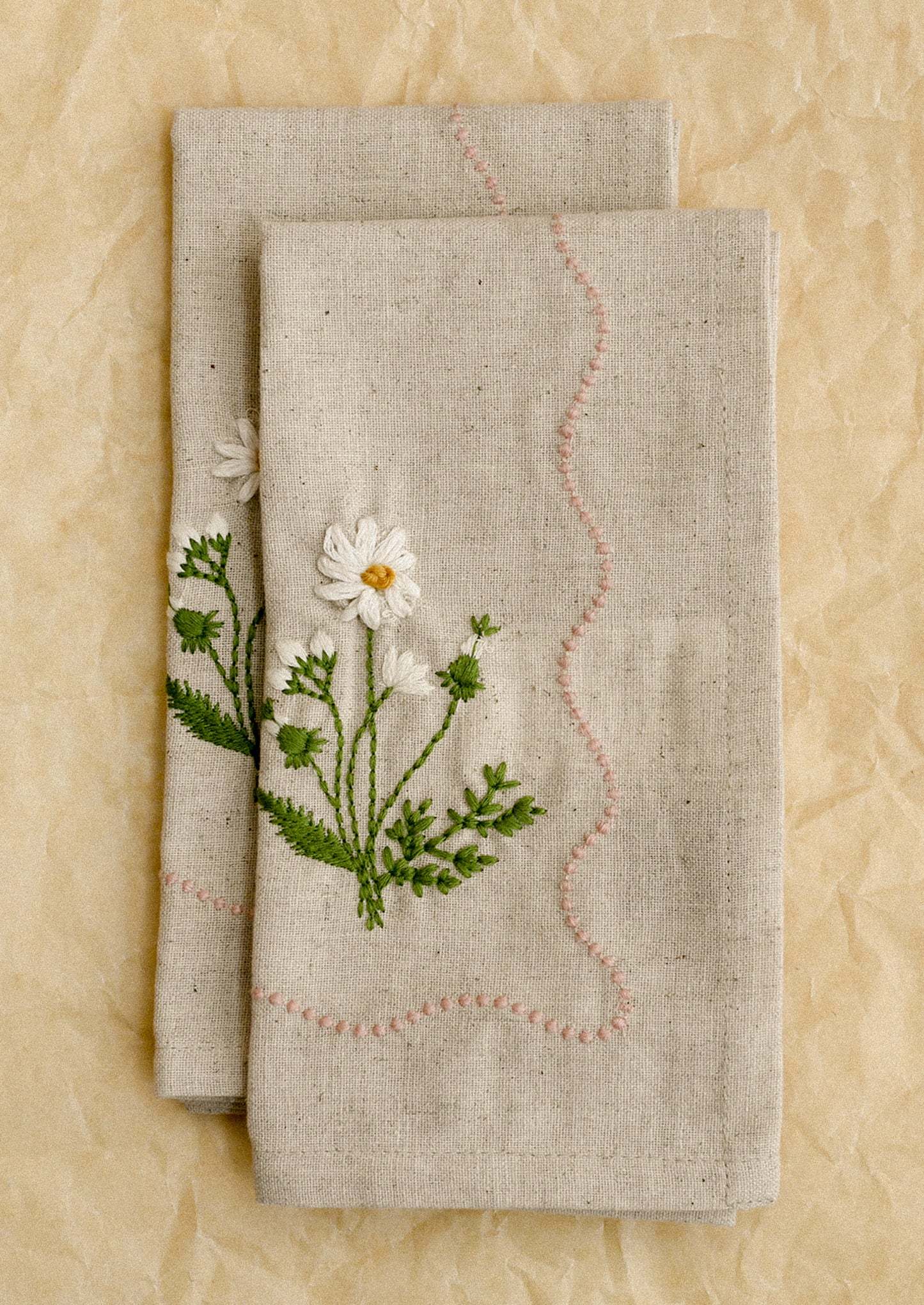 Two linen napkins with floral embroidery on a beige background