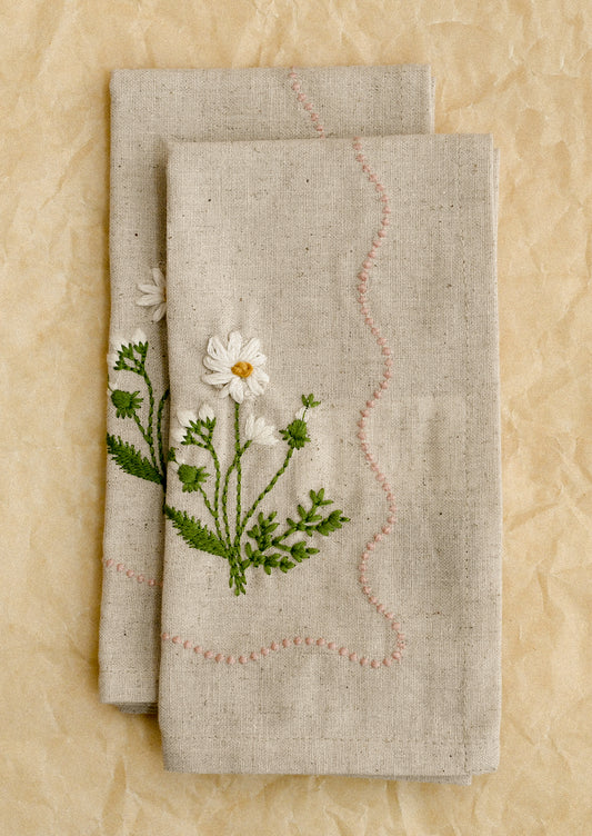 Two linen napkins with floral embroidery on a beige background