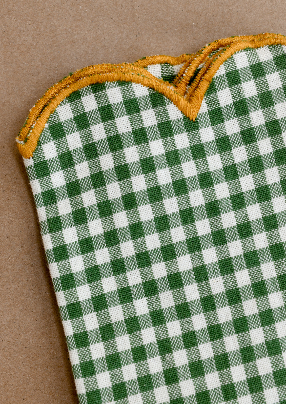 Green and white checkered cloth napkins with scalloped edges on a brown background