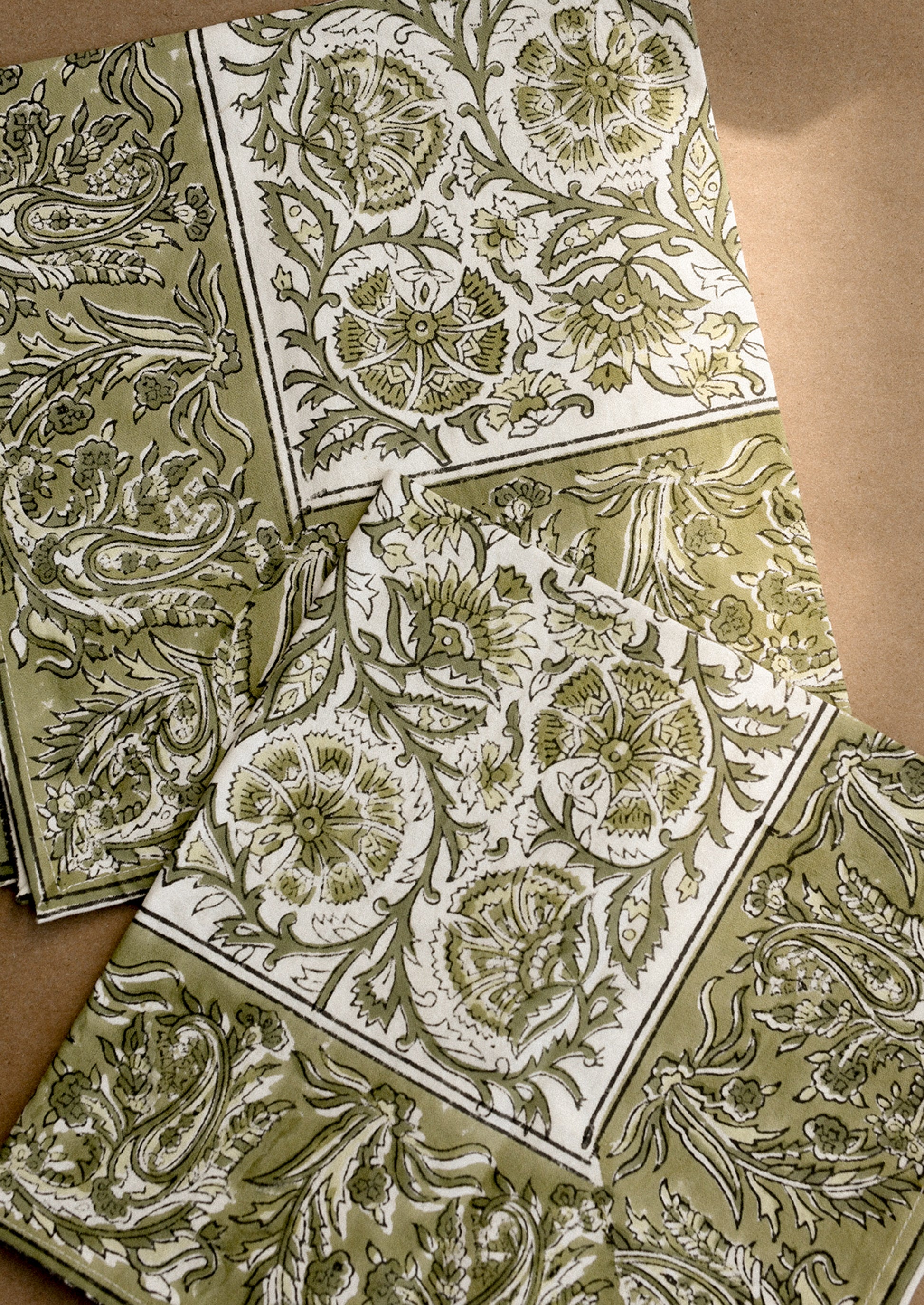 A set of cloth napkins in green and white traditional floral block print pattern.