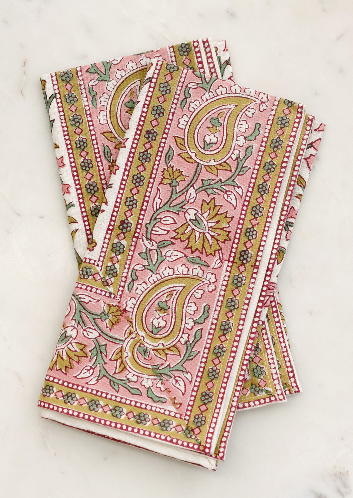 A set of cloth napkins in pink and mustard paisley print.