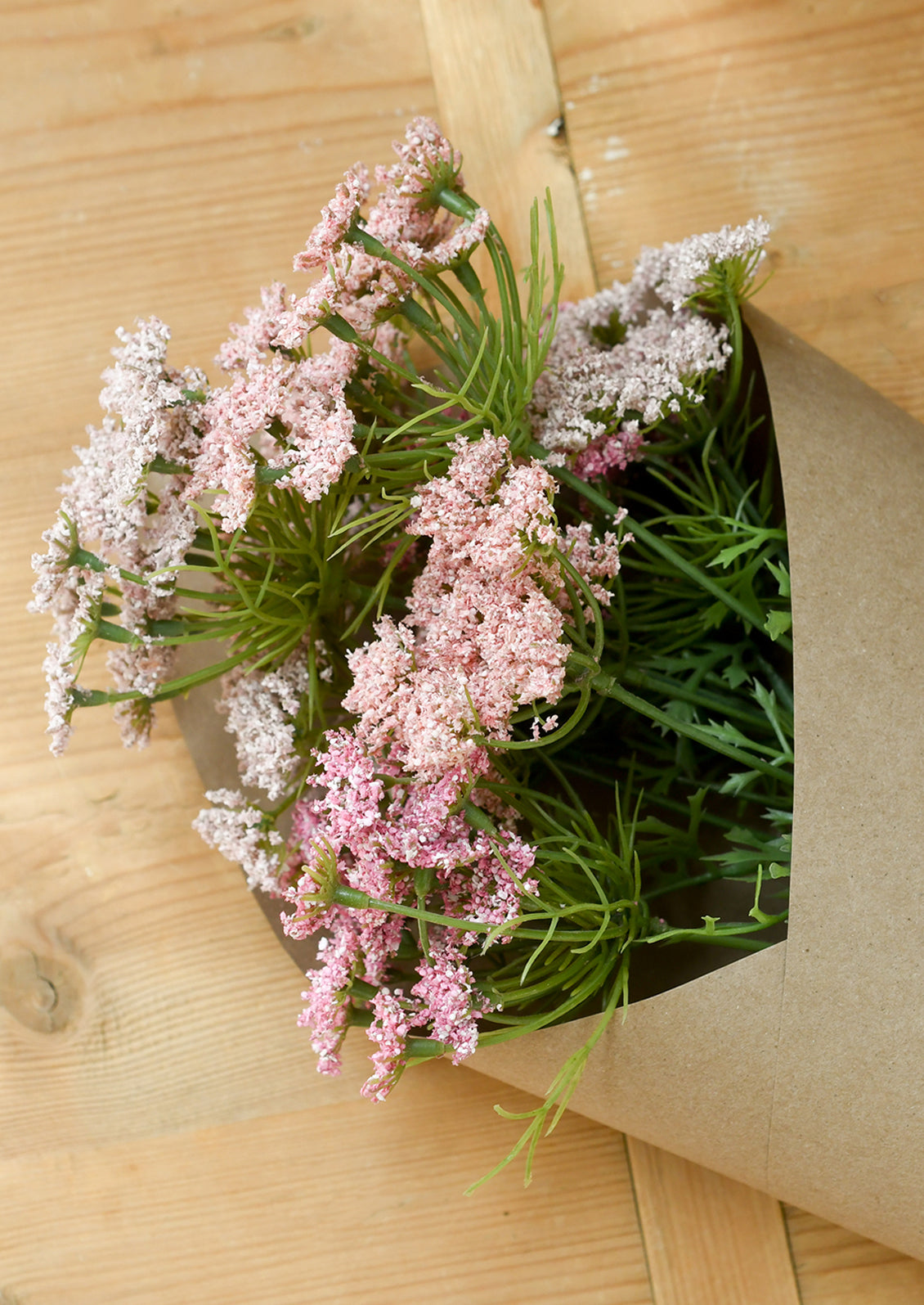 Bouquet of pink flowers in brown paper on a wooden surface