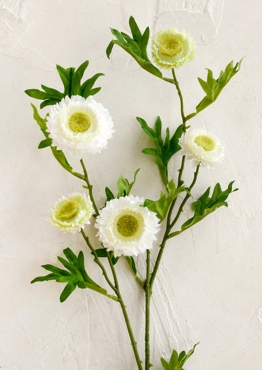 Artificial flower branch with white flowers and green leaves on a light background