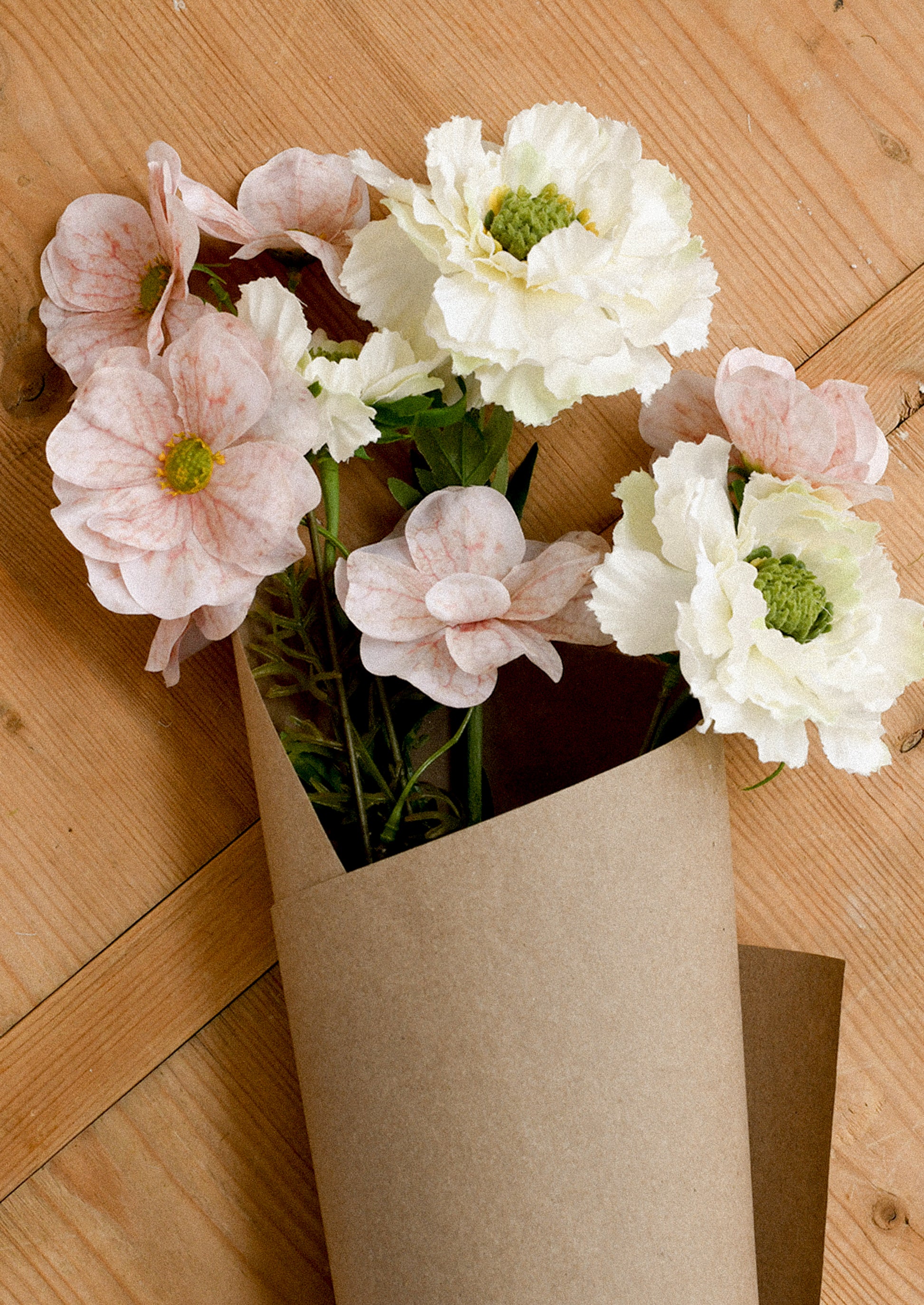 Bouquet of pink and white flowers in a brown paper bag on a wooden surface