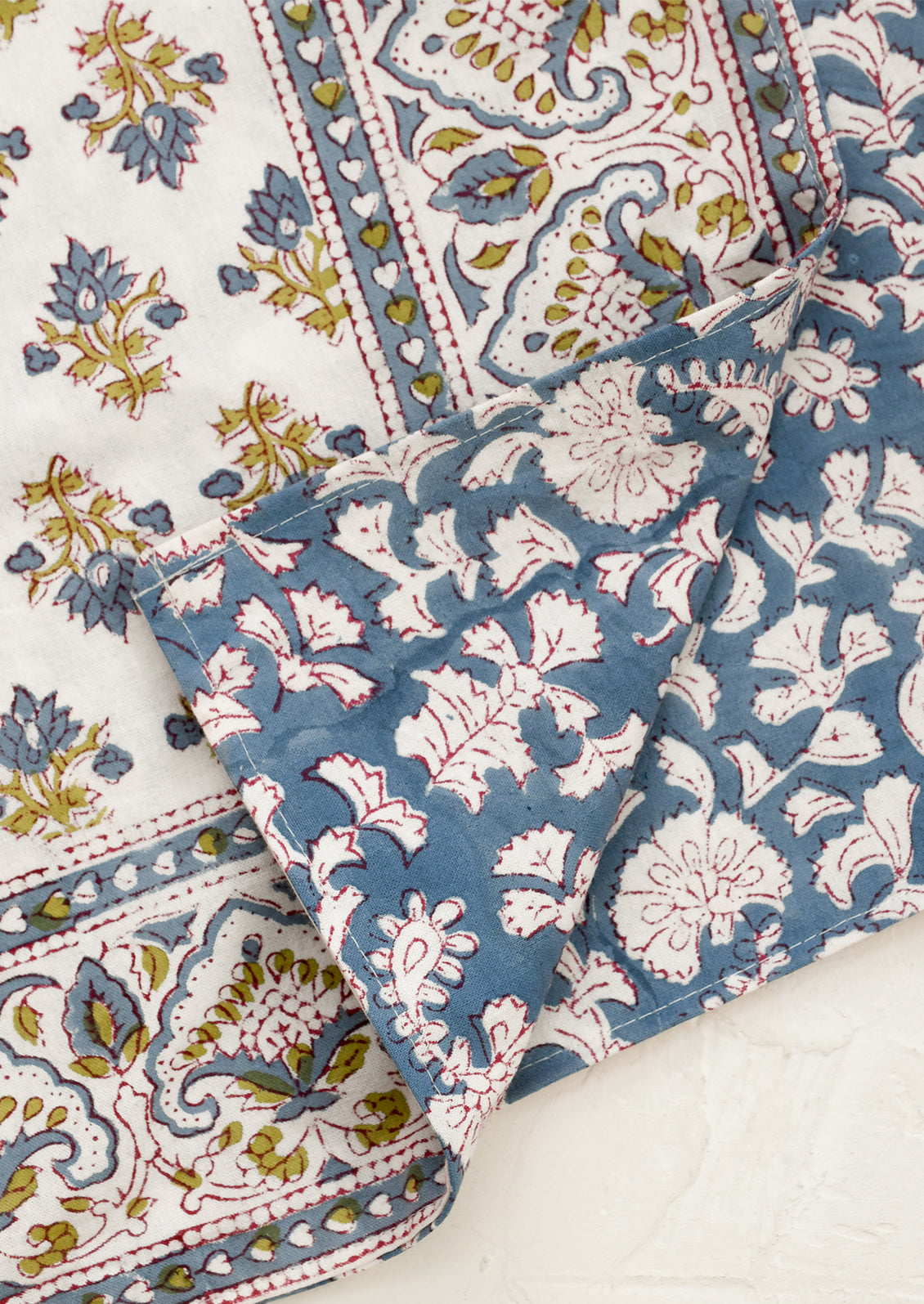 Patterned fabric with floral and paisley designs in blue, white, and pink on a white background.