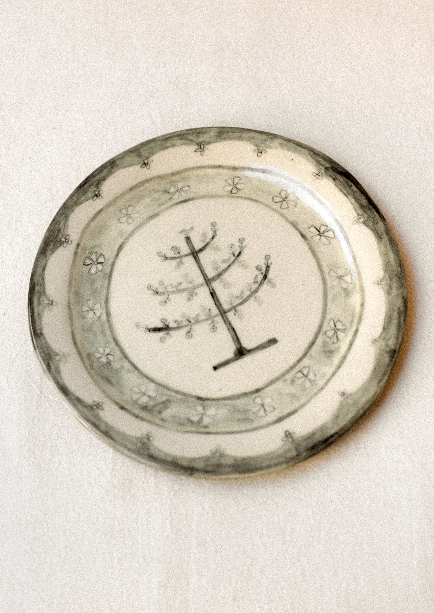 A cream ceramic plate with illustrated tree and flowers in dark grey.