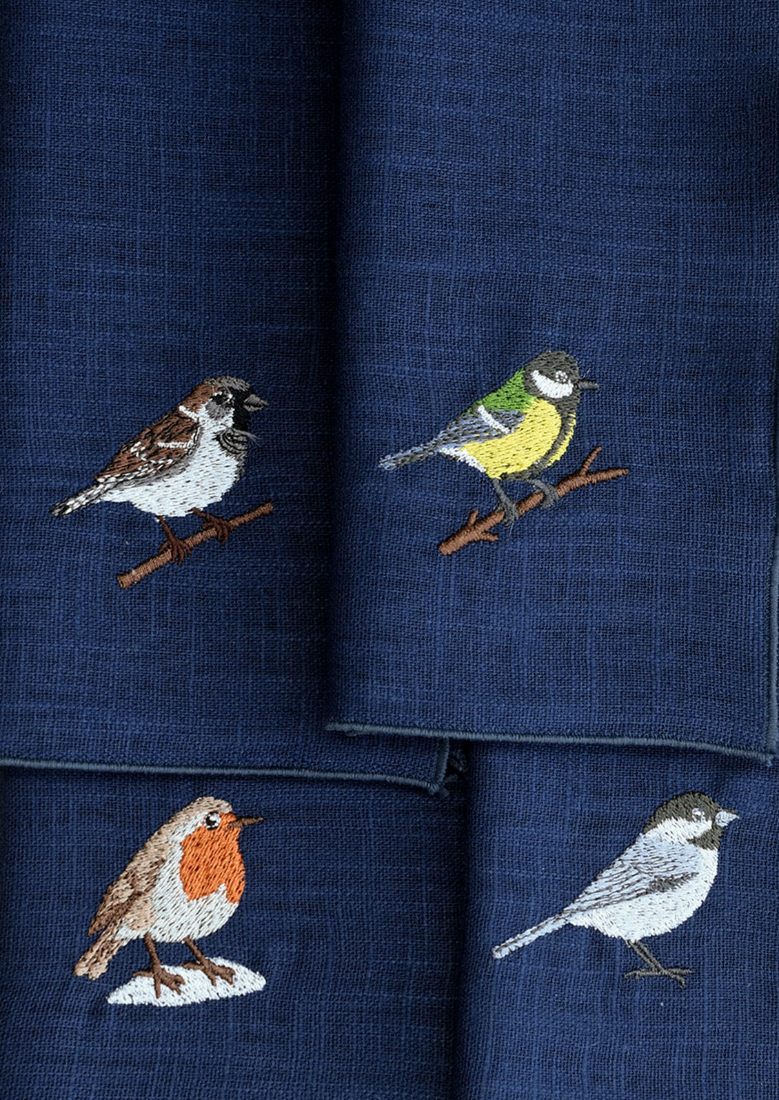 Navy blue linen napkins in four different styles of embroidered bird motifs.