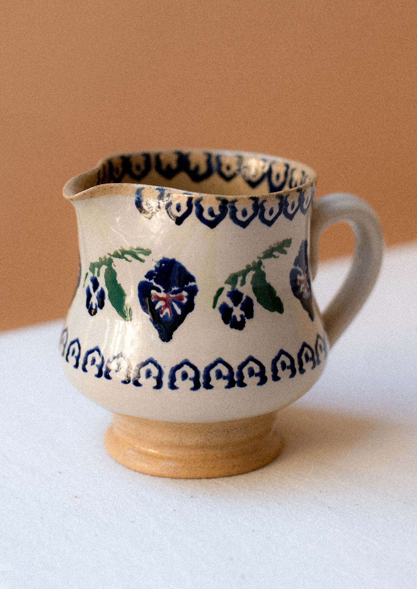 A ceramic pitcher with hand painted pansy floral pattern.