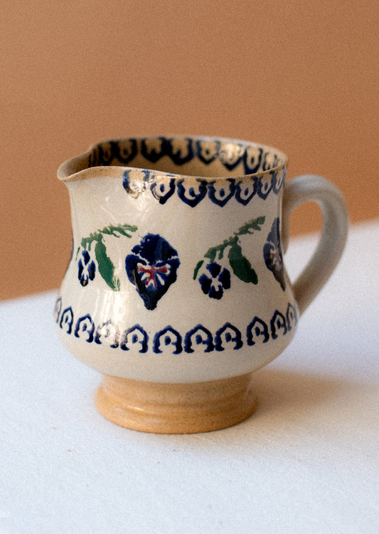 A ceramic pitcher with hand painted pansy floral pattern.