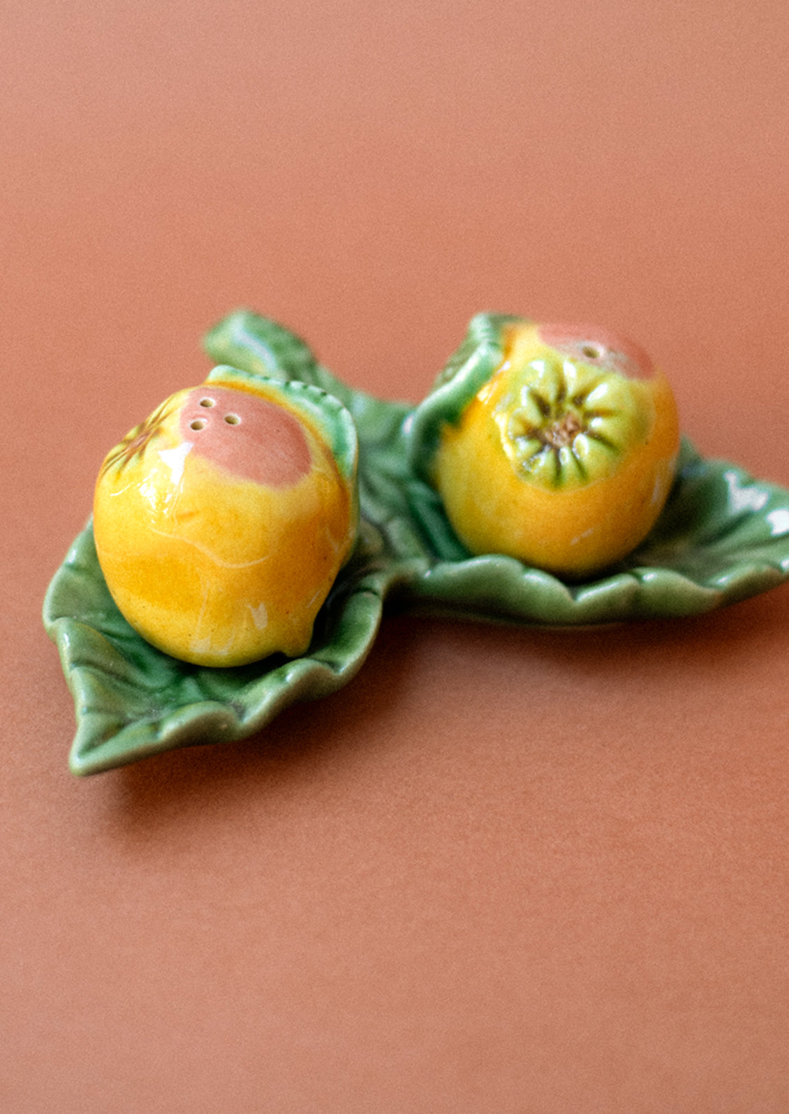 A pair of salt and pepper shakers in the form of a grapefruit, resting on leaf-shaped tray.