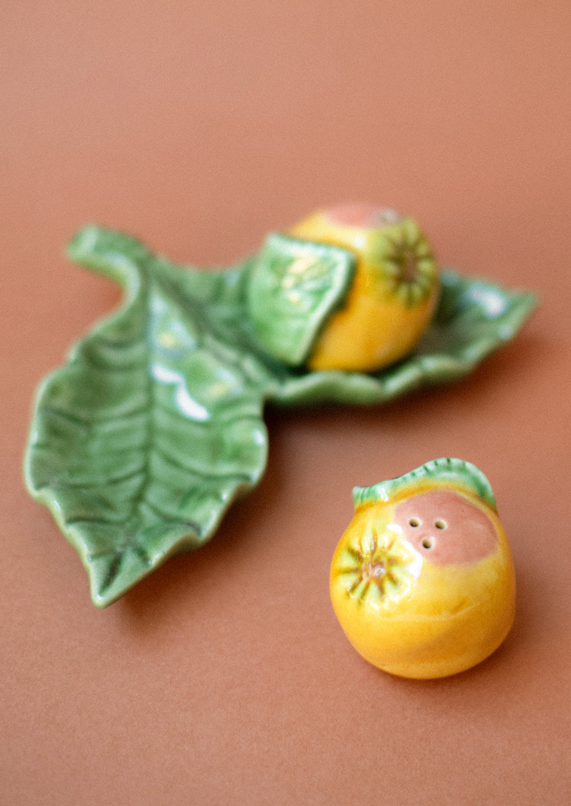 A pair of salt and pepper shakers in the form of a grapefruit, resting on leaf-shaped tray.