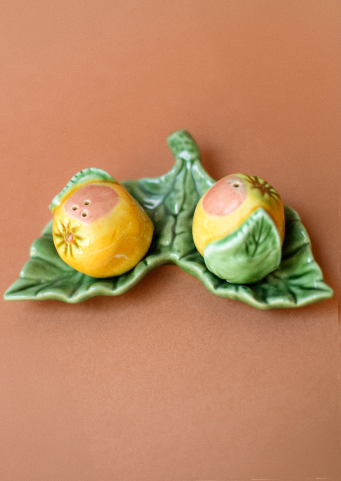 A pair of salt and pepper shakers in the form of a grapefruit, resting on leaf-shaped tray.