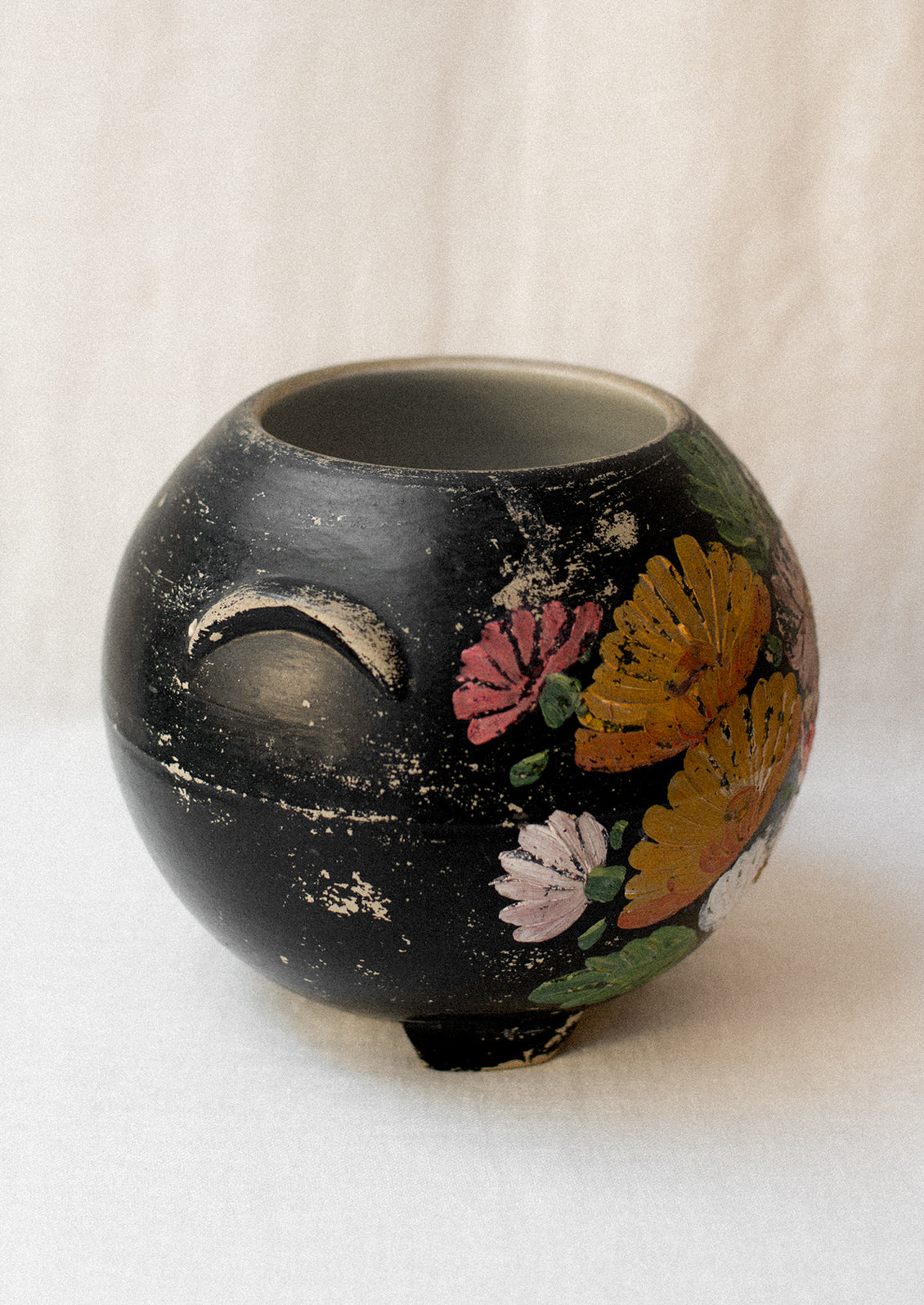 A black lidless round crock with multicolor aster flower pattern.