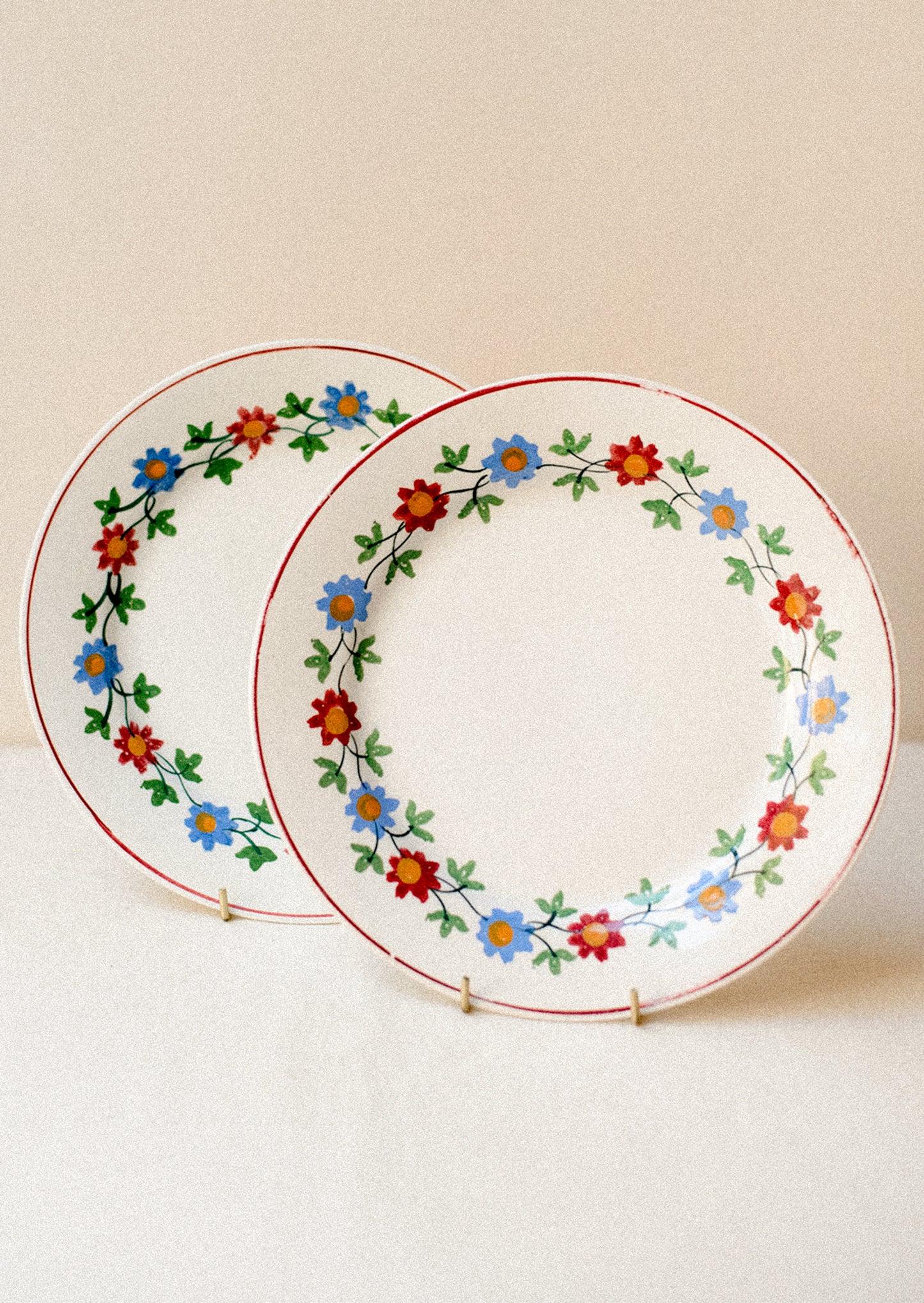 A pair of white plats with blue and red floral pattern around rim.