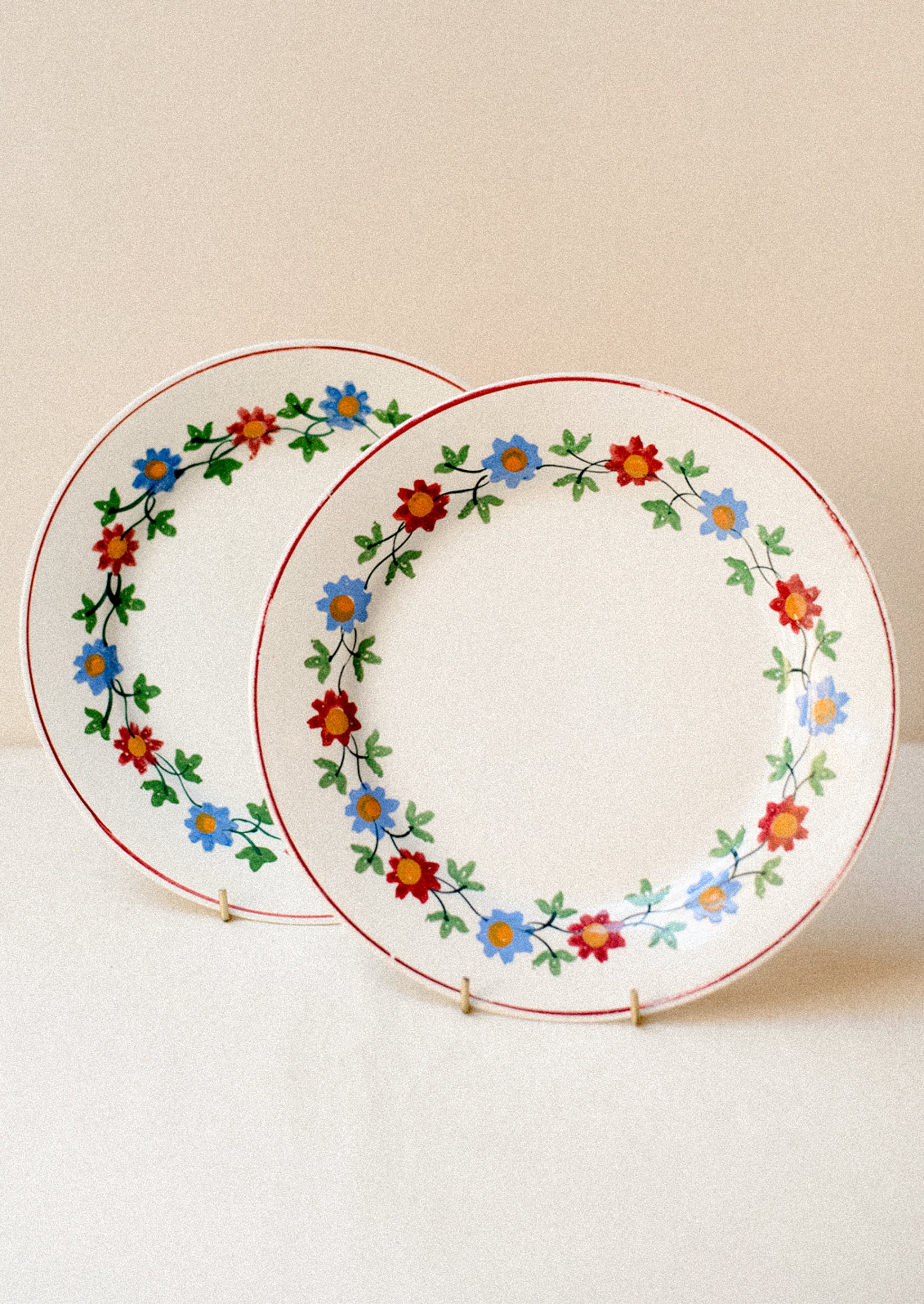 A pair of white plats with blue and red floral pattern around rim.