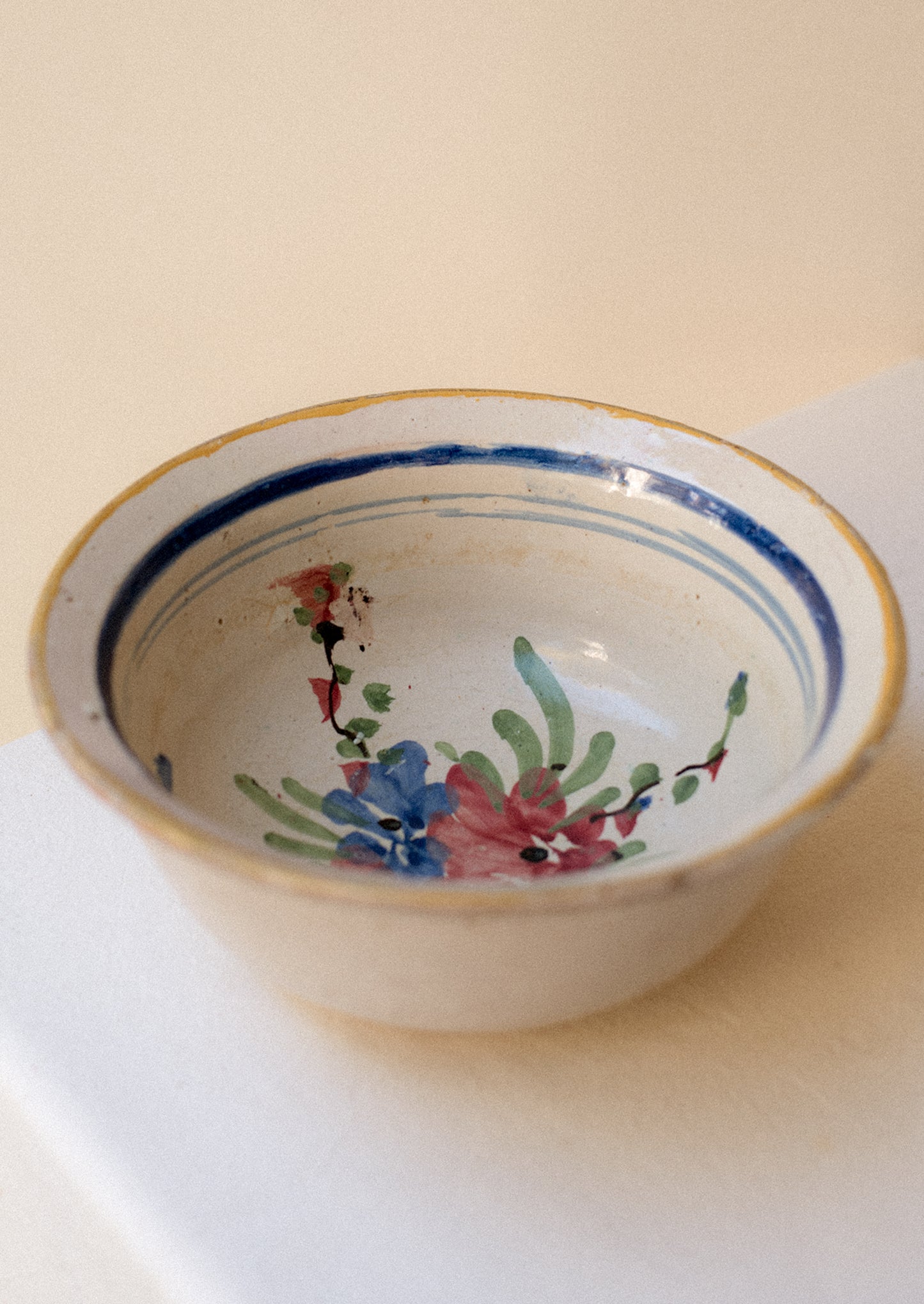 An antique ceramic serving bowl with painted blue rim and pink floral pattern.