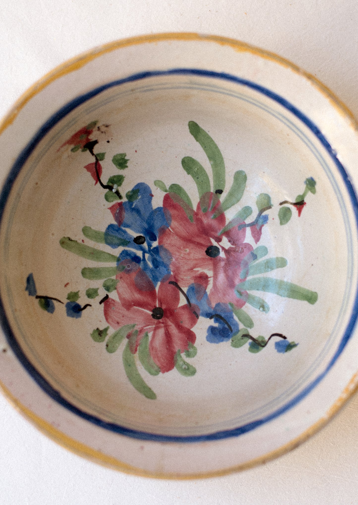 An antique ceramic serving bowl with painted blue rim and pink floral pattern.