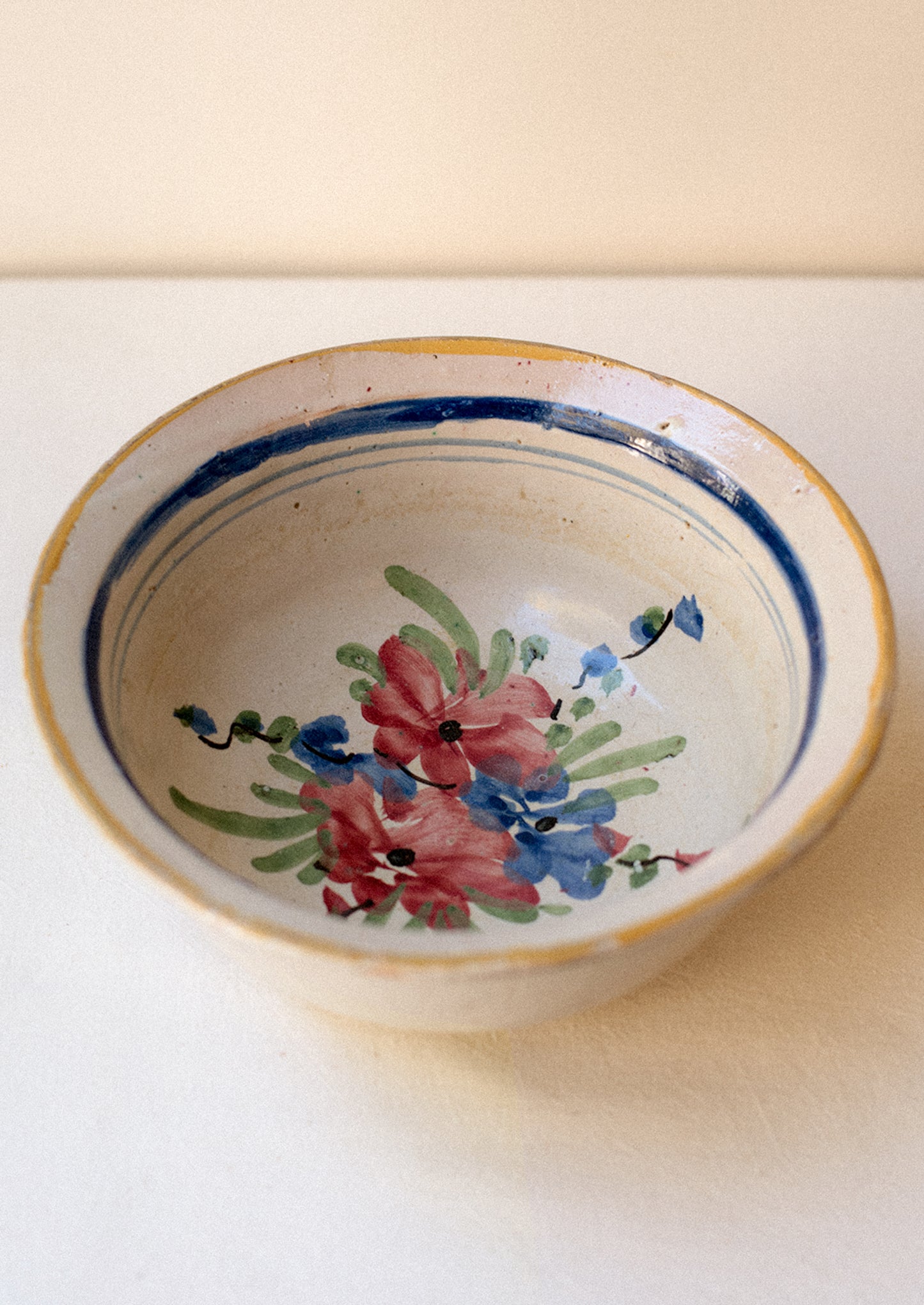 An antique ceramic serving bowl with painted blue rim and pink floral pattern.