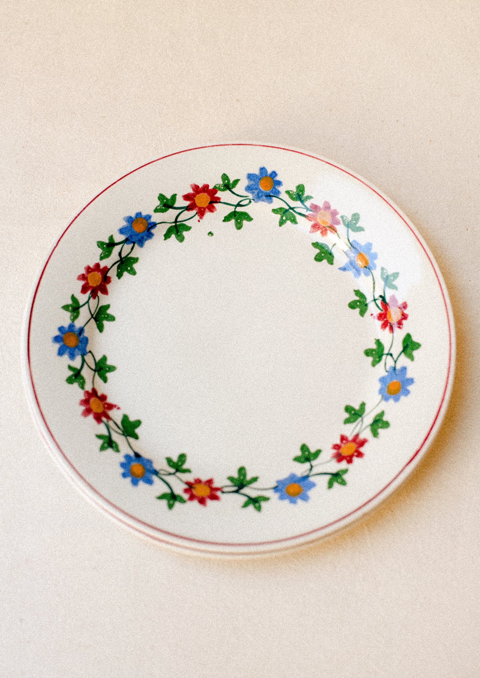 A pair of white plates with blue and red floral pattern around rim.