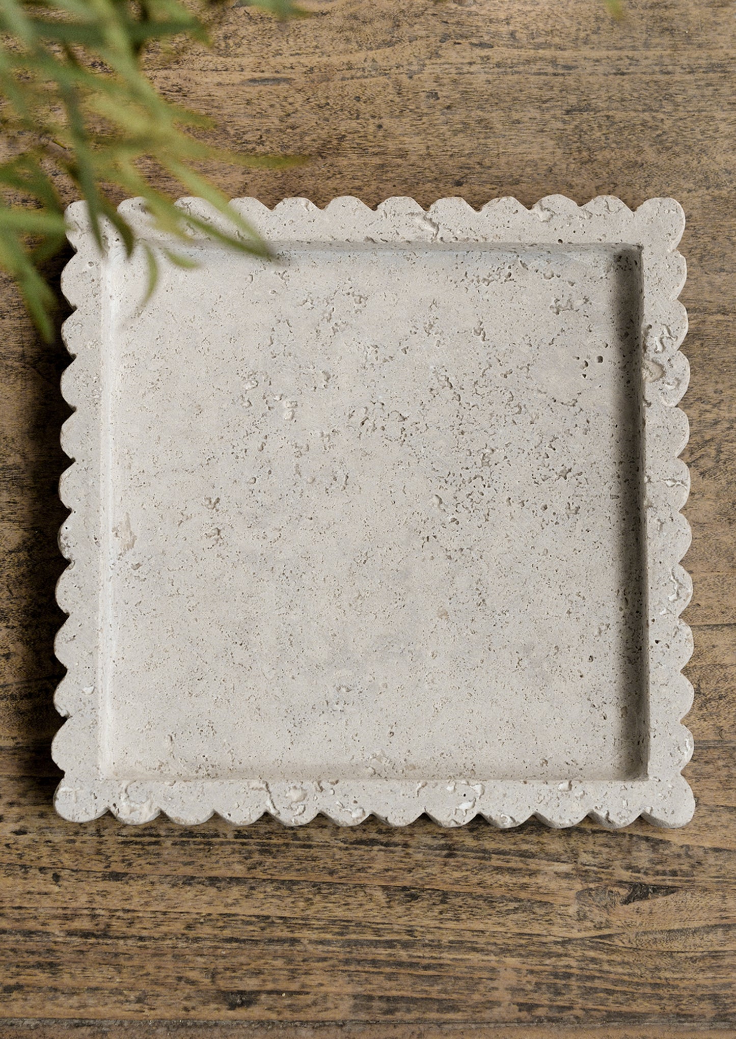 A square shaped travertine tray with scalloped edges.