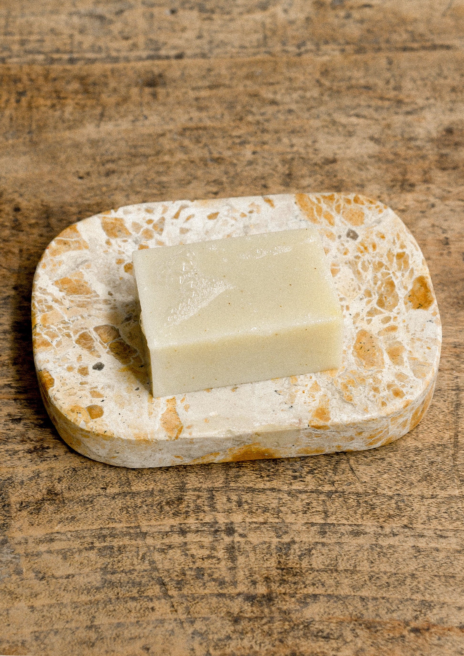 A tan marble soap dish holding a bar of soap.