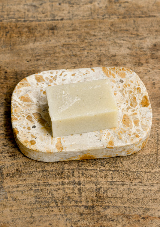 A tan marble soap dish holding a bar of soap.