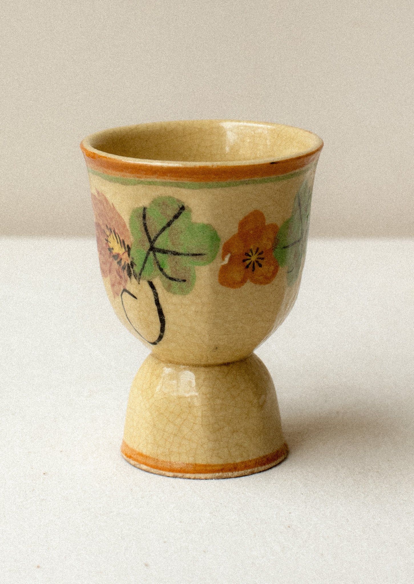 An antique egg cup in tan ceramic with caramel colored trim, and nasturtium floral pattern.