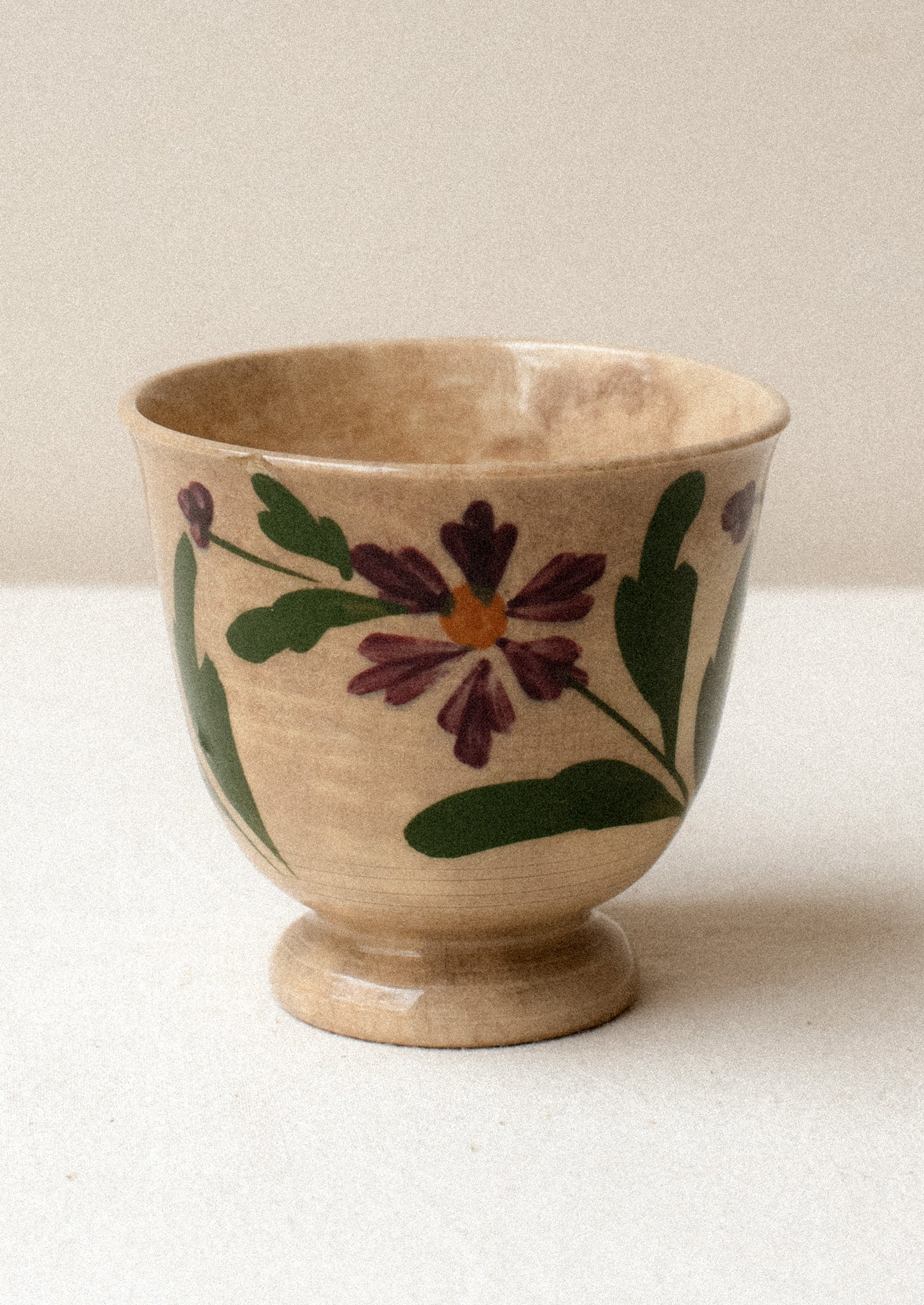 A tan ceramic antique tea cup with purple floral pattern.